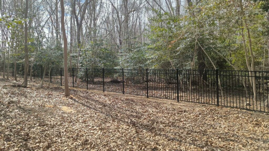 A black metal fence installed in a wooded area by Fence Pros Direct in Saunderstown, RI.