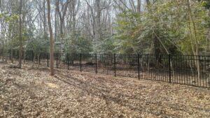 A black metal fence installed in a wooded area by Fence Pros Direct in Saunderstown, RI.