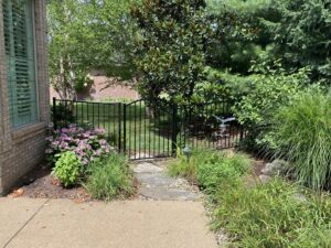 A black ornamental metal fence and gate installed in a lush garden area by Nailed It Fencing and Exteriors in Evansville, IN.