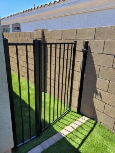 A black metal gate installed between two block walls leading to an area with artificial turf by Competitive Fence Contractors LLC in Scottsdale, AZ.