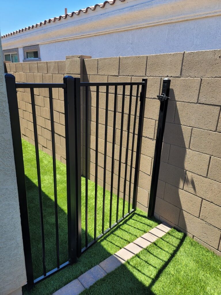 A black metal gate installed between two block walls leading to an area with artificial turf by Competitive Fence Contractors LLC in Scottsdale, AZ.