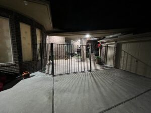 A black metal fence enclosing a large patio and driveway area at night, installed by GOAT Fence Company in Houston, TX.