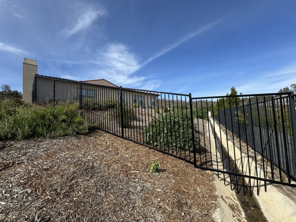 A black metal perimeter fence installed on a sloped property by Gates Access Solutions in San Diego, CA