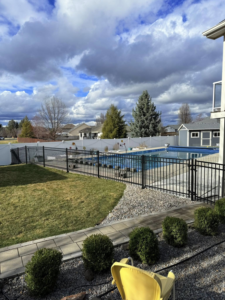 A black metal fence enclosing a swimming pool, with a white privacy fence in the background, by BKC Fencing in Spokane, WA.