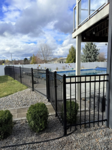 A black metal pool fence gate with a white privacy fence in the background, installed by BKC Fencing in Spokane, WA.