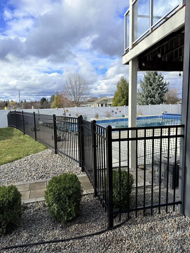 A black metal pool fence gate with a white privacy fence in the background, installed by BKC Fencing in Spokane, WA.