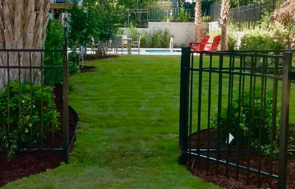 A black metal fence with an open gate providing access to a pool area, installed by Charleston Fencing Services in Moncks Corner, SC.