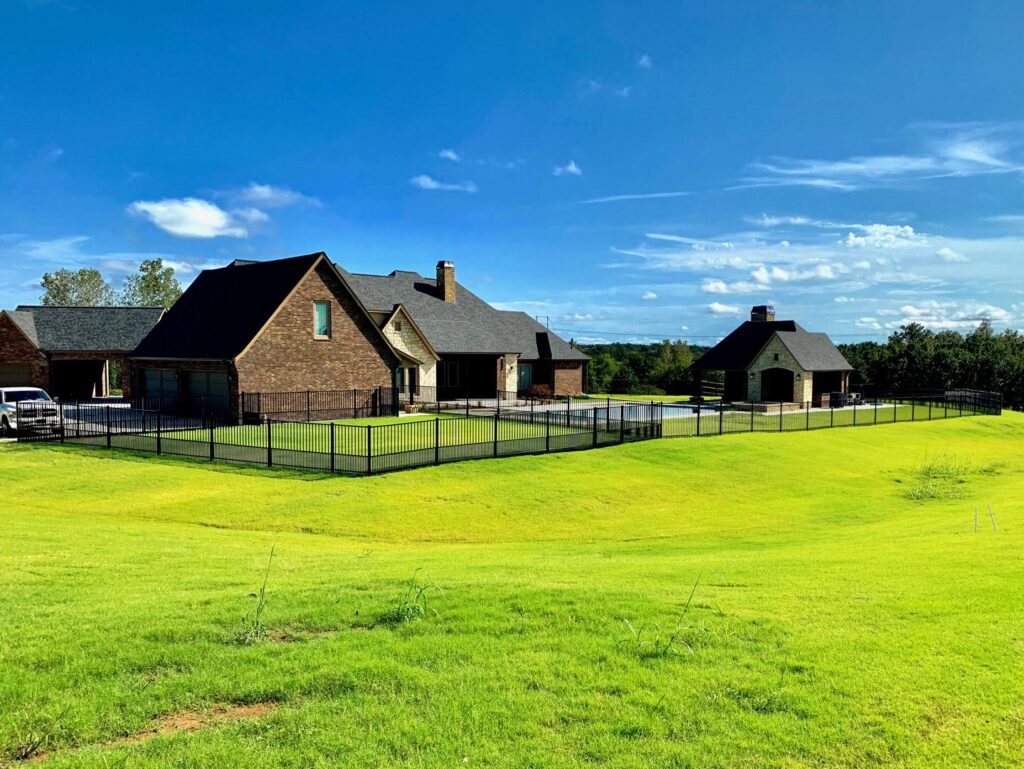 A black metal fence enclosing a pool area and large backyard on a residential property by Ninety-One Services in Tulsa, OK