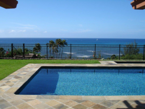 A black metal fence surrounding a swimming pool with an ocean view, installed by Allied Security Fence in Kapolei, HI