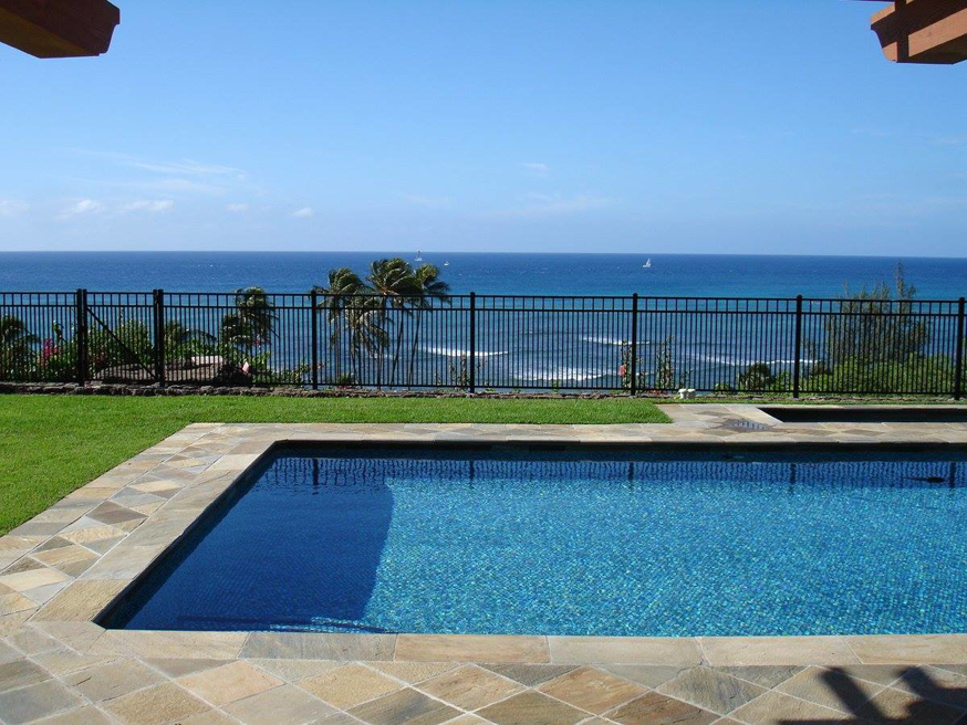 A black metal fence surrounding a swimming pool with an ocean view, installed by Allied Security Fence in Kapolei, HI