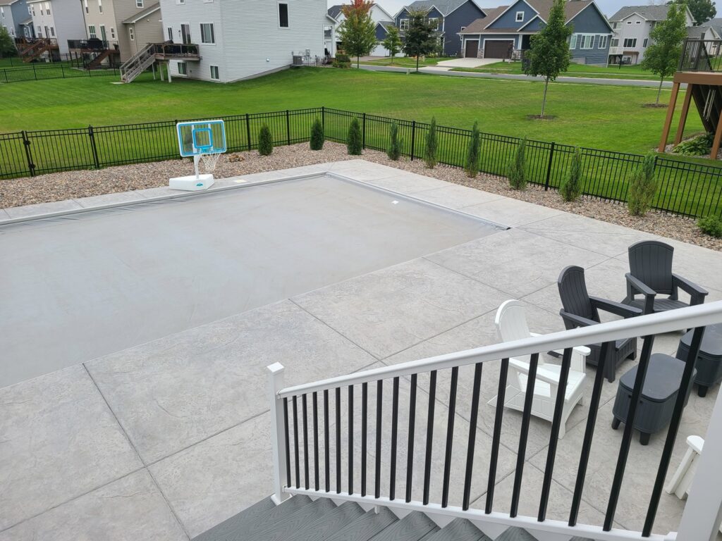 A black metal fence enclosing a pool and patio area with outdoor furniture, installed by Mauer Company in Little Canada, MN.