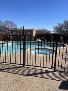 A black metal fence with a gate enclosing a swimming pool area by Backyard Builders in Rockford, MI.