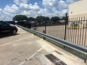A black metal security fence installed along a parking lot with a guardrail by BAR Z Fencing and Welding LLC in Midlothian, TX