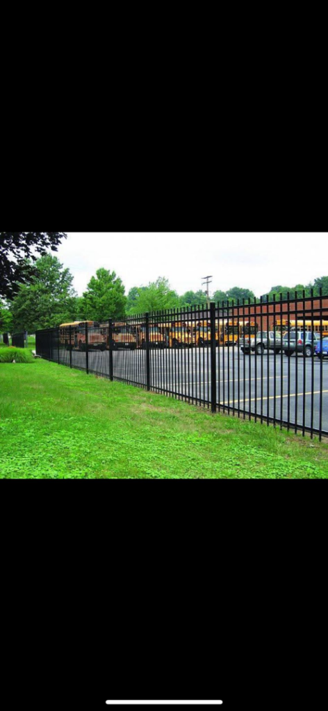 A long black metal security fence installation by Gonzalez Iron Work in Oakland, CA, separating a grassy area from a parking lot.