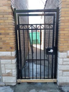 A black metal security gate installed between two brick walls by Superior Custom Fence Inc. in Chicago, IL.