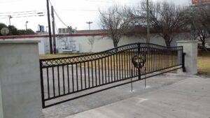 A custom black metal sliding gate with concrete pillars and a 'PHO' logo, installed by Serrato's Fence & Welding in San Antonio, TX.