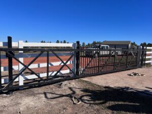 A large black metal sliding gate with white ranch-style fencing installed by Western Fence in Hebron, ND.