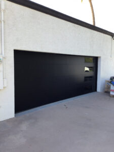 A sleek black modern garage door installed on a white stucco residential home by Overhead Door Company of Maricopa & Pinal County in Mesa, AZ.
