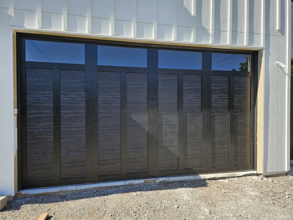 A black modern garage door with horizontal windows on a white house by Babcock Garage Doors in Vancouver, WA