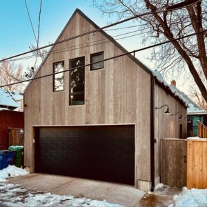 A sleek black modern garage door installed on a wooden-sided house by Colorado Garage Door Pro's in Denver, CO