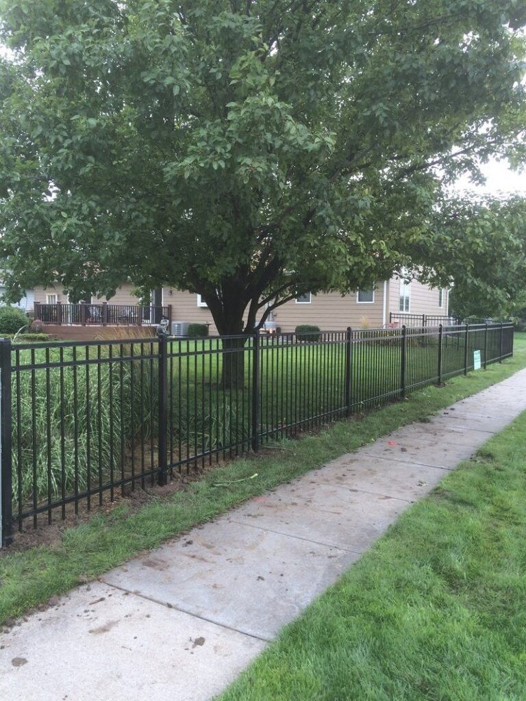 A black ornamental aluminum fence installed along a residential sidewalk by Schumacher Fencing, LLC in Columbus, NE.