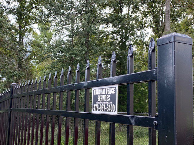 A black ornamental fence with a National Fence Services, LLC sign, demonstrating quality fencing in Macon, GA.