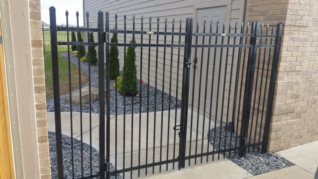 A black ornamental fence with a gate installed next to a brick building by Sharper Image Fence in Fort Wayne, IN.