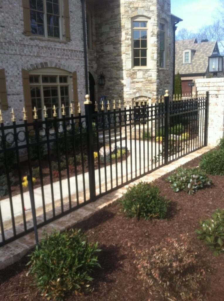 A black ornamental metal fence with decorative gold finials bordering a walkway by Georgia Select Fence in Senoia, GA.