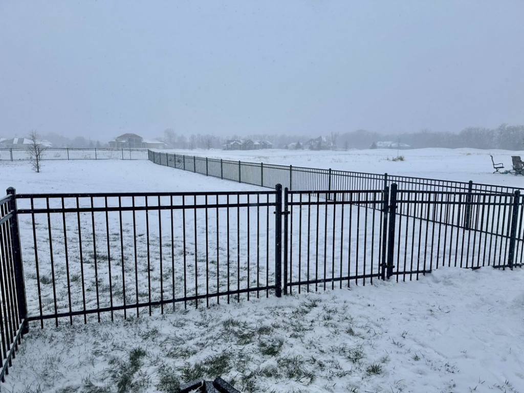 A black ornamental fence with a gate installed in a snowy backyard by JD Fencing LLC in Boone, IA.