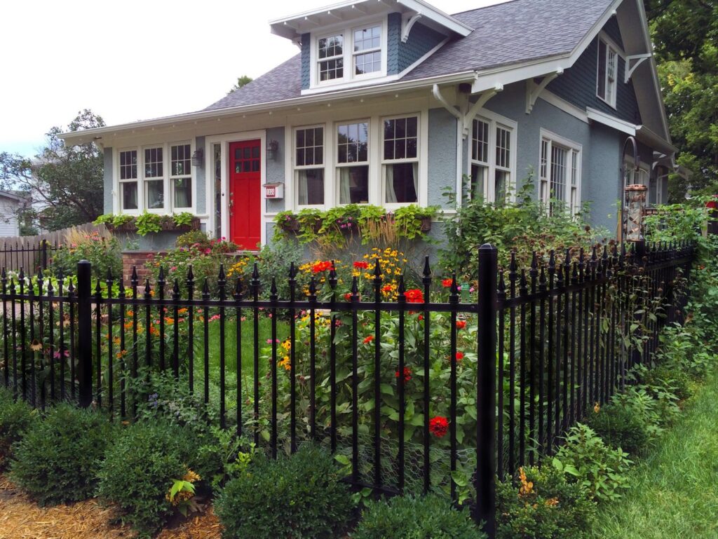 A black ornamental fence enclosing a vibrant garden in front of a house, installed by American Fence Company - Omaha in Omaha, NE.