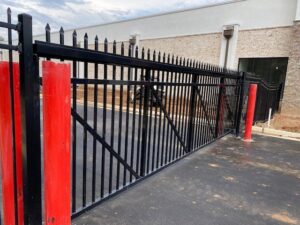A robust black ornamental gate with red safety bollards at a commercial entrance, installed by National Fence Services, LLC in Macon, GA.