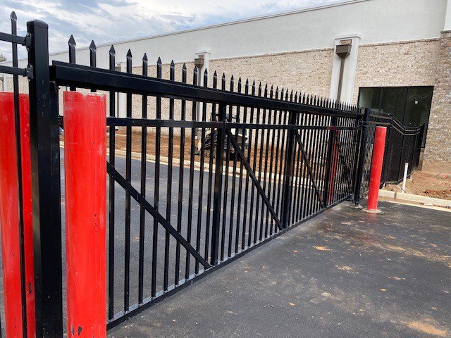 A robust black ornamental gate with red safety bollards at a commercial entrance, installed by National Fence Services, LLC in Macon, GA.
