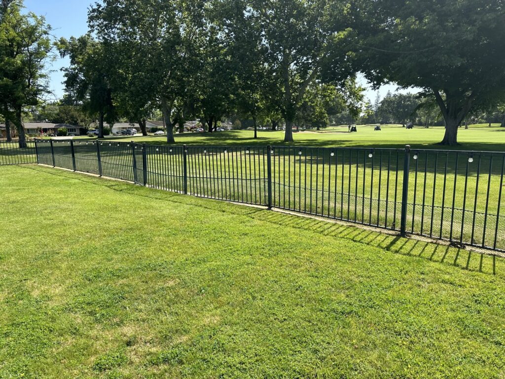 A durable black ornamental iron fence bordering a green park or golf course, installed by Mega Fence in Thornton, CA.