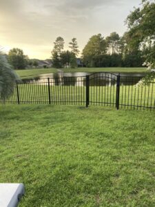 A black ornamental iron fence with a gate installed along a pond in a backyard by Crompton Fence Company in Charleston, SC.