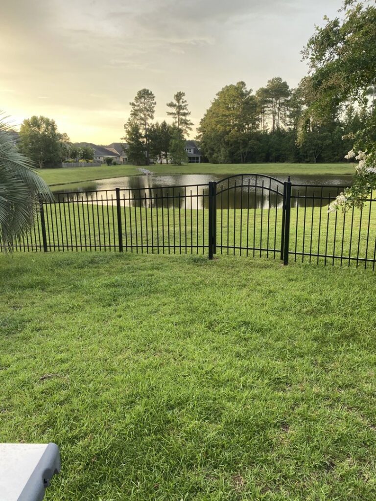A black ornamental iron fence with a gate installed along a pond in a backyard by Crompton Fence Company in Charleston, SC.