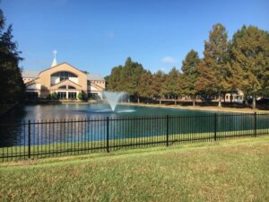 A black ornamental iron fence installed around a pond with a building in the background by Texas Fence and Iron Co. in Houston, TX.