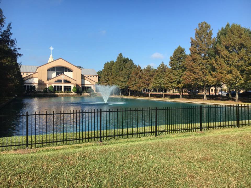 A black ornamental iron fence installed around a pond with a building in the background by Texas Fence and Iron Co. in Houston, TX.