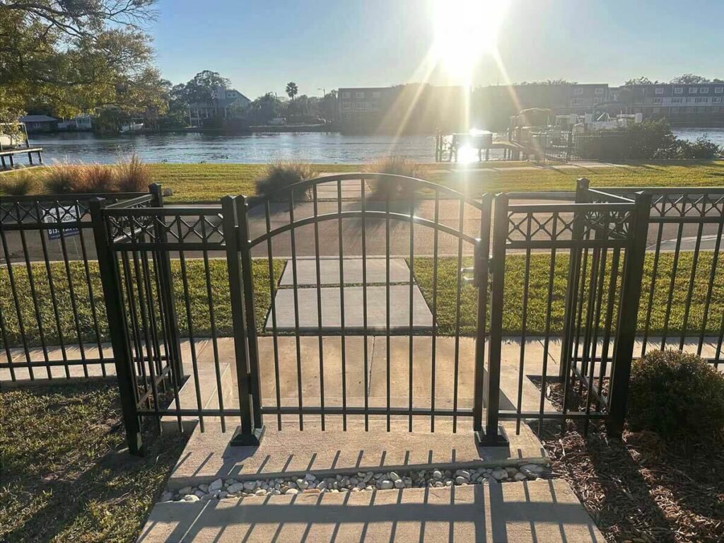 A black ornamental metal fence with an arched gate overlooking a waterfront, installed by Golden Eagle Fencing in Tampa, FL