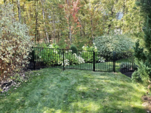 A black ornamental metal fence installed in a lush garden setting, enhancing aesthetics by Dirigo Fence Company in Augusta, ME.