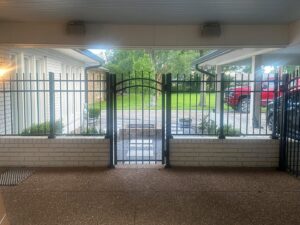 A black ornamental fence with a gate installed on a white brick wall by Nash Fence & Supplies Inc. in Lake Charles, LA.