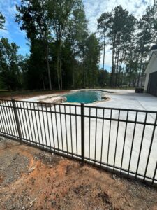 A black ornamental metal fence surrounding a swimming pool with a concrete deck by Georgia Select Fence in Senoia, GA.