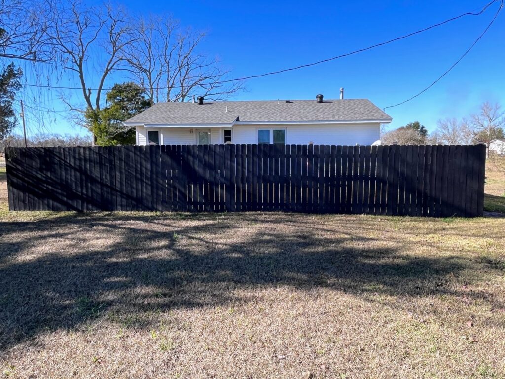 A newly installed black painted wooden privacy fence in a field by Dallas' Custom Carpentry in Alexandria, LA.