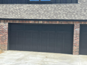 A modern black panel garage door installed on a brick house by L & S Overhead Door in Tulsa, OK.