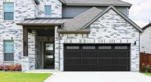 A black panel garage door with top windows installed on a modern residential house by Overhead Doors Unlimited, LLC in Appleton, WI.