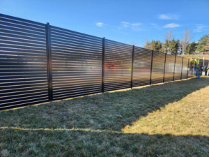 A newly installed black slatted fence in a grassy area by Van's Fence in Kansas City, MO.