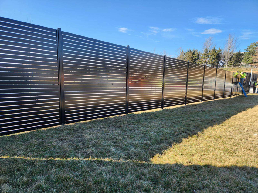 A newly installed black slatted fence in a grassy area by Van's Fence in Kansas City, MO.