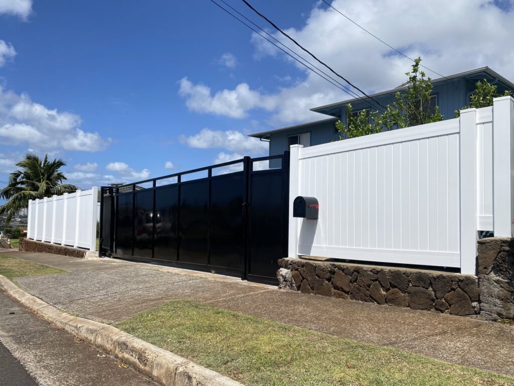 A long black sliding gate installed alongside a white vinyl fence by A&D Services in Kapolei, HI.