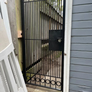 A black metal security gate with vertical bars and decorative rings, installed by Fierro Iron Works Inc. in San Francisco, CA.