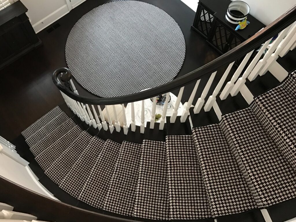 A black and white patterned carpet runner on a spiral staircase with a matching round rug by Carpet Binding Company in Charlotte, NC.