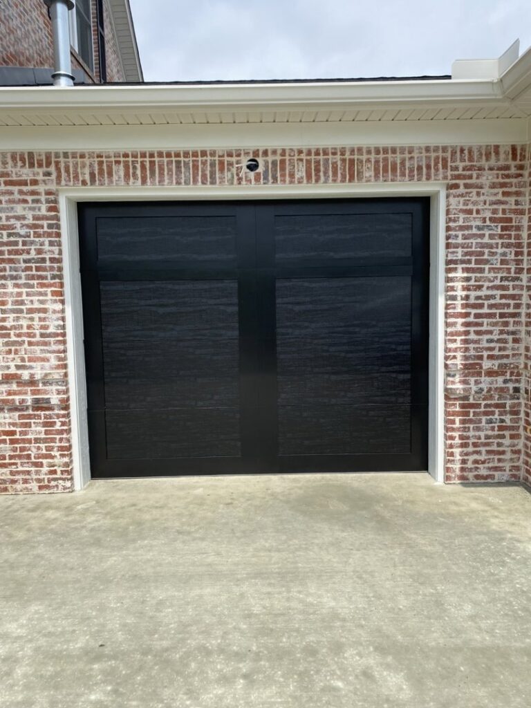 A black wood-look garage door installed on a brick house by Smith's Garage Door in Clarksville, TN.